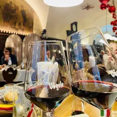 Dwa kieliszki pełne ciemnoczerwonego lagrein wino, w tle restauracja z ludźmi i świątecznymi ozdobami.