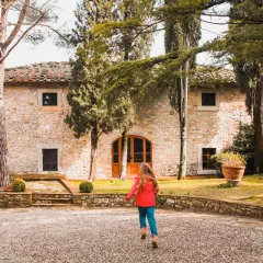 Dziecko biegnie do kamiennego domu w Castello di Ama, otoczonego drzewami i zielenią.