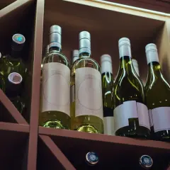 Butelki białego wina w drewnianym regale. Zastanawiasz się, czy szampan może się przeterminować? Te butelki czekają na degustację.