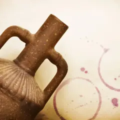 Starożytne naczynie na wino, z dwoma uchwytami, stoi obok śladów po kieliszkach.