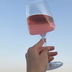 Różowe letnie wino w kieliszku, unoszone na tle błękitnego nieba. Idealny moment na orzeźwienie.