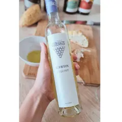Dłoń trzyma butelkę lodowego wina Eiswein Exquisit z Austrii. Na stole leży chleb i miseczka z oliwą.