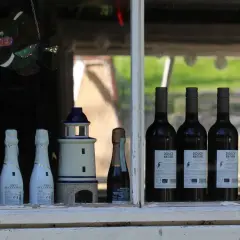 Na parapecie okna stoją butelki wina i szampana. Widać latarenki, witrażową rybę i kontretykietę wina z napisem "Douce Nature".