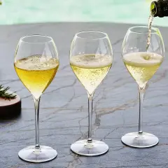Trzy kieliszki wypełnione musującym winem. Jedno z nich jest nalewane z butelki. To jest właśnie cava!