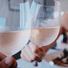 Dwie osoby wznoszą kieliszki z różowym winem, na których widać delikatny biały nalot.