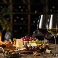 Degustacja najlepszych win: kieliszki z czerwonym i białym winem, deska serów, winogrona, oliwki i świece tworzą nastrojową atmosferę.