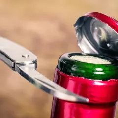 Metalowy widelec próbuje otworzyć wino, podważając kapsel. Zaskakujący sposób na otwarcie butelki, gdy brakuje korkociągu.