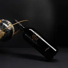 Elegancka butelka Sessantanni Primitivo di Manduria, otoczona złotym pierścieniem, obok globusa.
