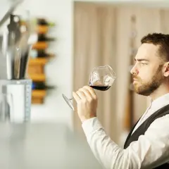 Mężczyzna, degustator win, wącha kieliszek czerwonego wina, oceniając jego aromat.