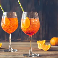 Dwa orzeźwiające drinki Aperol Spritz z plastrami pomarańczy i kostkami lodu, ozdobione słomkami. Idealne na letnie popołudnie.