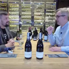 Dwóch mężczyzn przy stole degustuje wino. Na stole stoją butelki, w tym dwie z etykietami sugerującymi pinot noir.