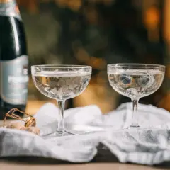Dwa kieliszki z musującym winem, jeden z borówkami, obok butelka i korek. Czy wino musujące to szampan?