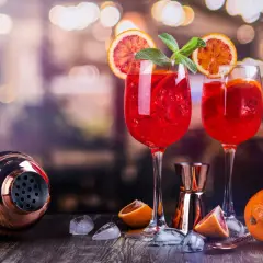 Dwa czerwone drinki z pomarańczą i miętą, idealne do prosecco. Obok shaker i pomarańcze.
