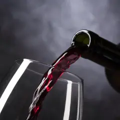 Ciemnoczerwone wino, być może najdroższe wino, leje się z butelki do kieliszka.