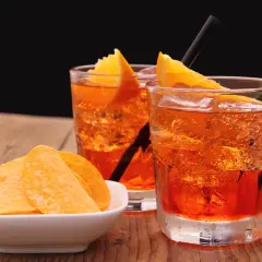 Dwa orzeźwiające drinki z pomarańczą i słomkami, obok miseczka chipsów. Idealne aperitif przykłady na letnie popołudnie.