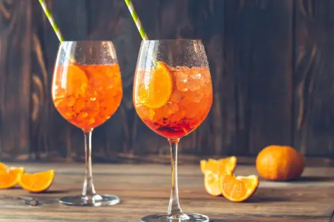Dwa orzeźwiające drinki Aperol Spritz z plastrami pomarańczy i kostkami lodu, ozdobione słomkami. Idealne na letnie popołudnie.
