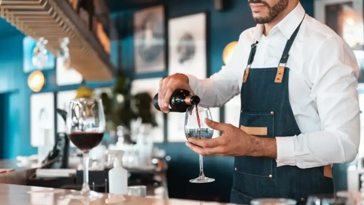 Doświadczony sommelier wina nalewa czerwone wino do kieliszka w eleganckiej restauracji.