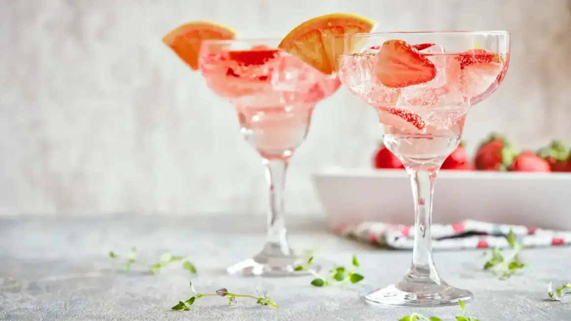 Orzeźwiające drinki z truskawkami i plasterkami grejpfruta, idealne na letnie popołudnie. W tle widać świeże truskawki.