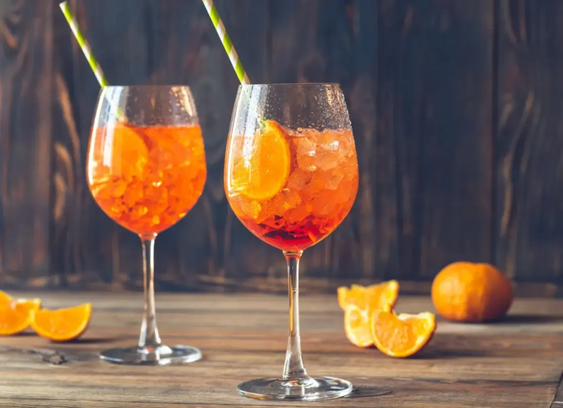 Dwa orzeźwiające drinki Aperol Spritz z plastrami pomarańczy i kostkami lodu, ozdobione słomkami. Idealne na letnie popołudnie.
