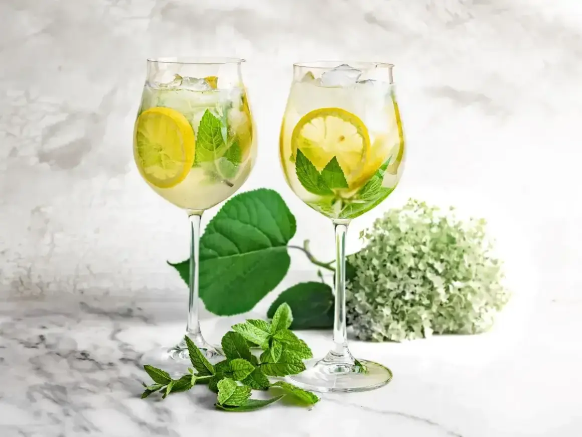 Orzeźwiający drink z prosecco i sokiem z bzu, ozdobiony plasterkami cytryny i listkami mięty, z lodem.