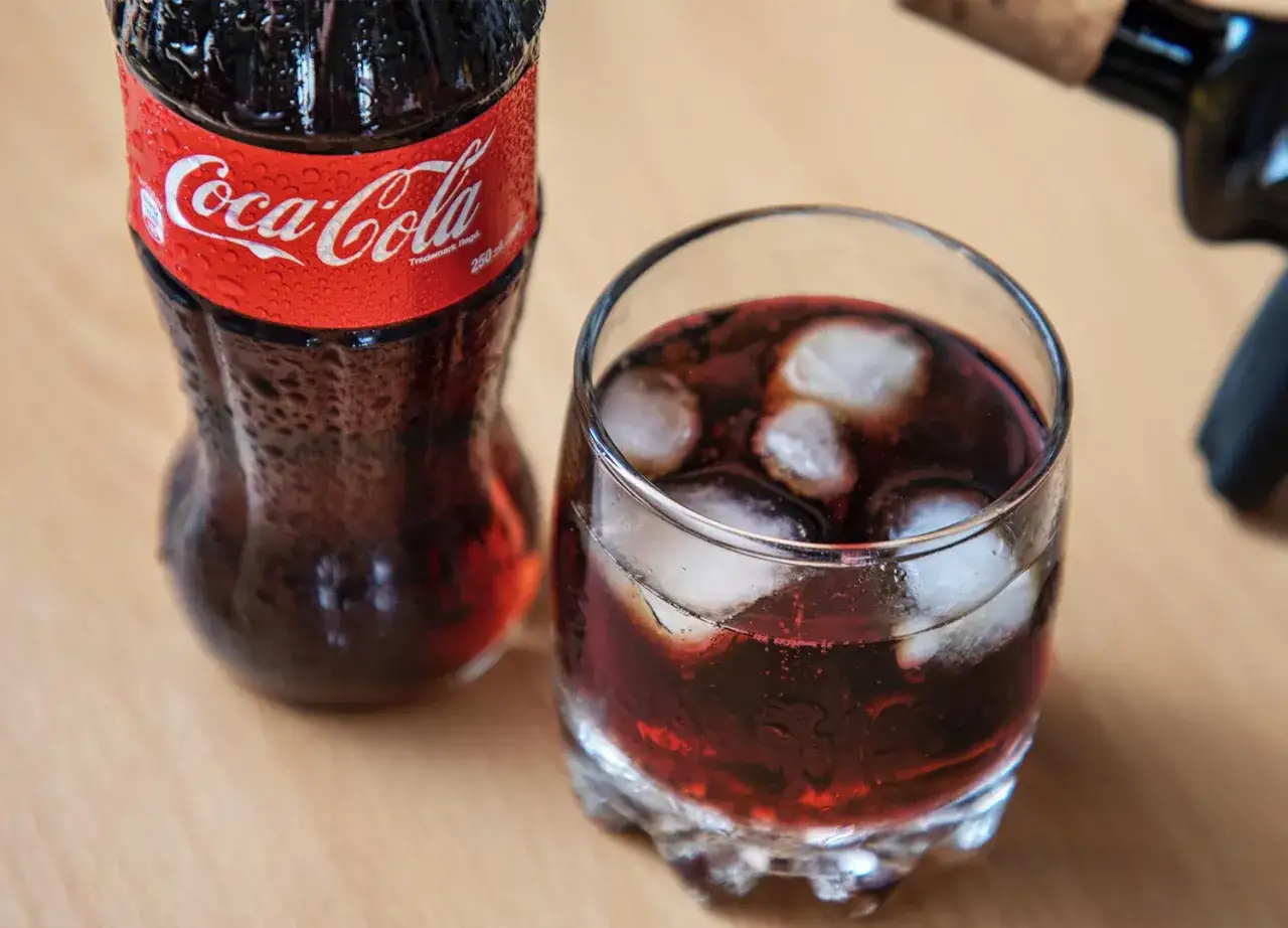 Szklanka z lodem i napojem, obok butelka Coca-Coli. Idealne na letnie orzeźwienie, gdy masz ochotę na wino z colą.