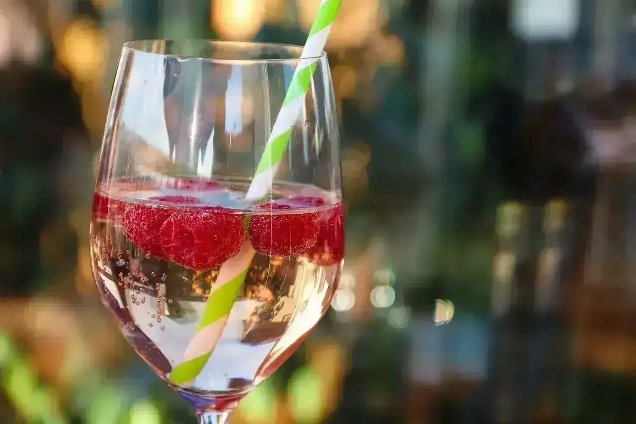 Orzeźwiające prosecco z malinami w kieliszku, ozdobione zielono-białą słomką. Idealne na letnie popołudnie.