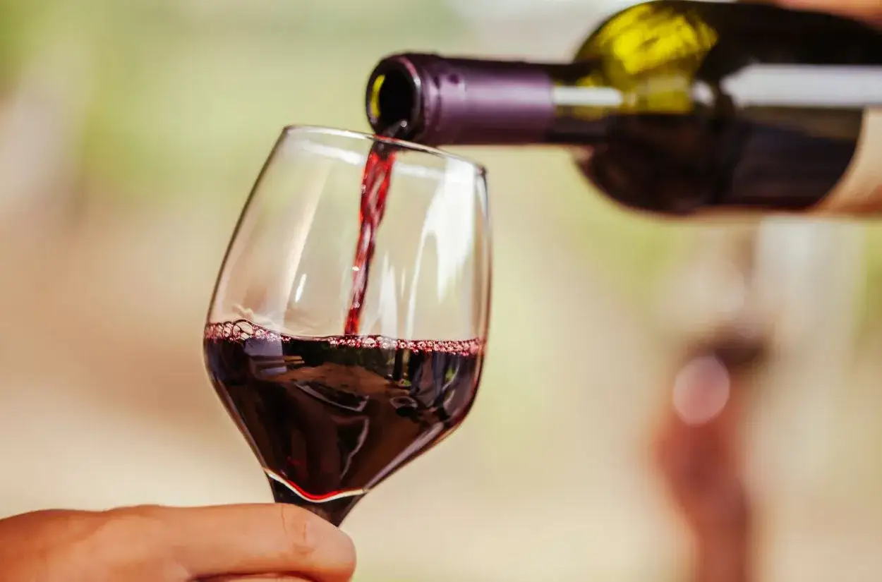 Ciemnoczerwone wino merlot leje się z butelki do kieliszka, tworząc bąbelki. To wino, które warto poznać!