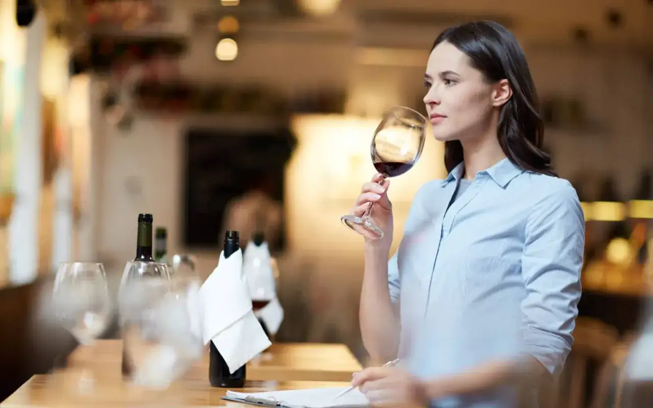Doświadczona sommelierka wina wącha bukiet czerwonego wina, notując wrażenia.