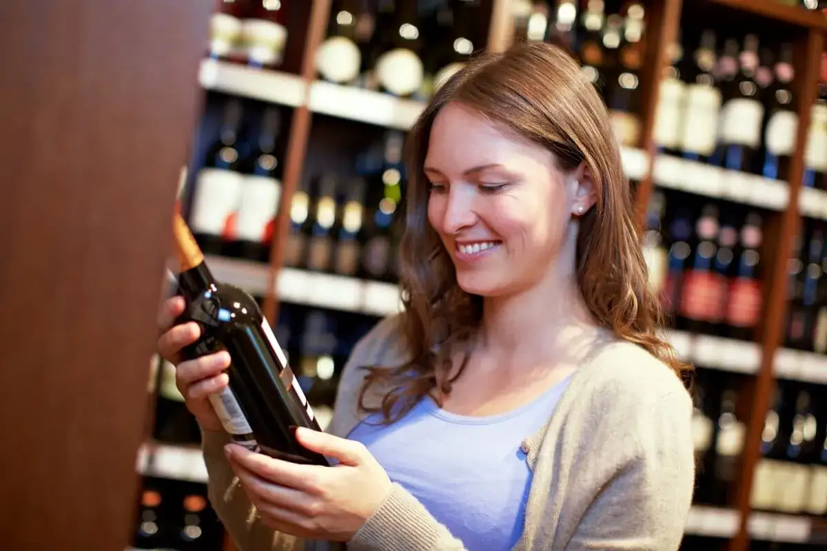 Uśmiechnięta kobieta wybiera wino w sklepie, jak prawdziwy sommelier.